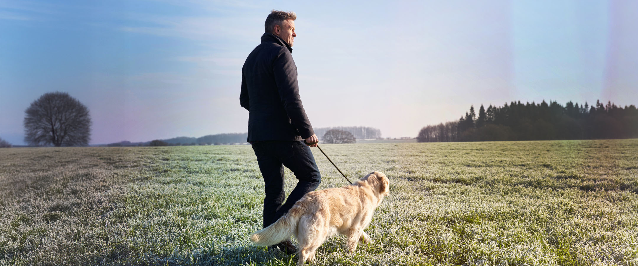 Man walking dog across frosty open field