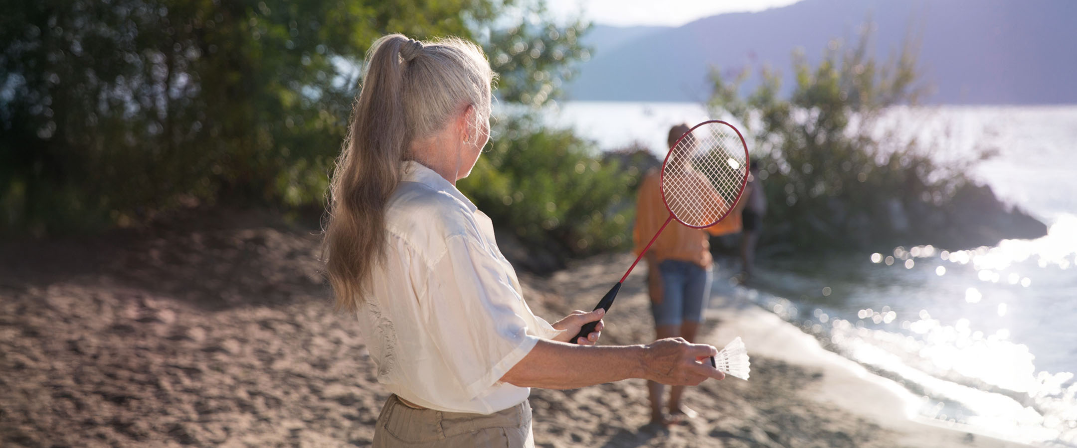 Senior woman playing badminton on lakeshore